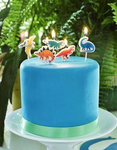 a blue cake with three candles on top of it and some animals in the middle