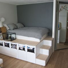 a bed sitting on top of a wooden floor next to a white shelf filled with pictures