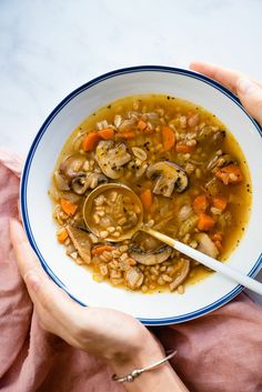 a person holding a spoon in a bowl filled with mushroom and barley soup on top of a pink blanket