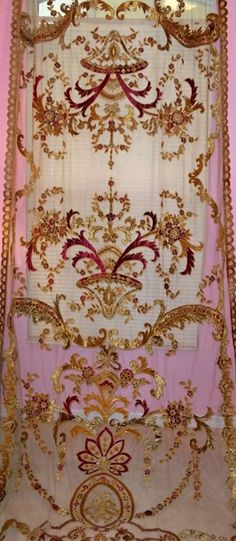 an ornate gold and red window curtain in a pink room