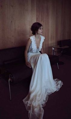 a woman in a white dress sitting on a black leather chair and looking off to the side