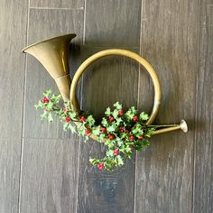 two brass horns with holly and red berries in them on a wood floor next to a glass vase