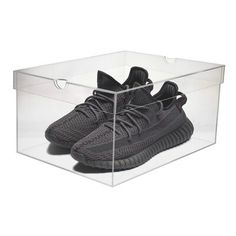 a pair of black adidas sneakers in a clear shoe box on a white background