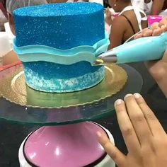 a person cutting a blue and pink cake on top of a table