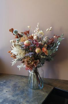 a glass vase filled with lots of flowers on top of a table next to a wall