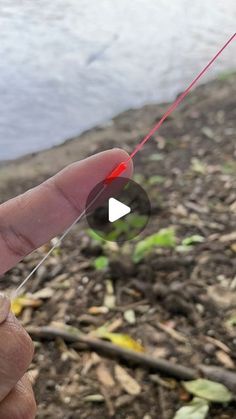 a hand holding a red string and pointing it at the camera with a river in the background