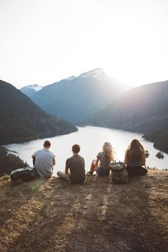 three people sitting on top of a hill overlooking a lake