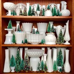 a wooden shelf filled with white vases and christmas trees