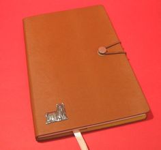 a brown leather notebook with a silver dog on the cover and a white stick sticking out of it