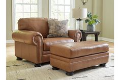 a brown chair and ottoman in a living room with a lamp on the side table