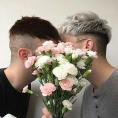 two young men kissing each other with flowers in front of them and one holding his face close to the camera