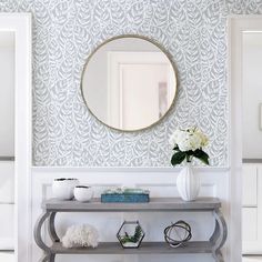 a console table with a mirror and vase on it in front of a wallpapered background