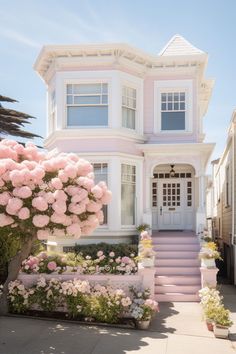 a large white house with pink flowers in the front yard and steps leading up to it