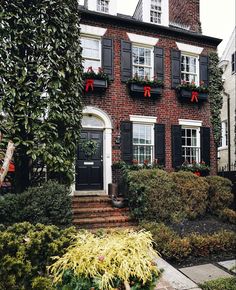 a red brick house with black shutters and christmas decorations on the front window boxes