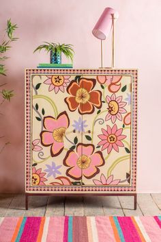 a cabinet with flowers painted on it and a pink lamp next to it in front of a pink wall