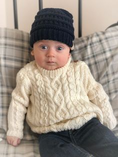 a baby wearing a hat and sweater sitting on a bed