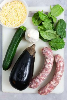 an assortment of vegetables on a cutting board with cheese, spinach and sausages