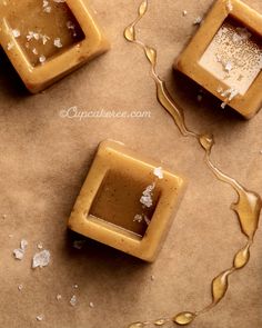 three square shaped desserts sitting on top of a piece of wax paper with white flakes around them