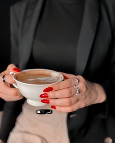 a woman holding a cup of coffee in her hands with red nails and black blazer