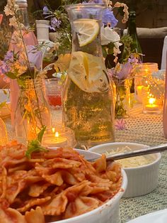 a table topped with lots of food and vases filled with lemonade next to candles