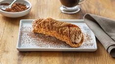 a pastry on a white plate with powdered sugar and coffee in bowls behind it