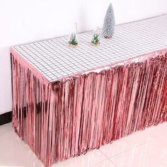 a table covered in pink tinsel next to a white wall with two small trees on top