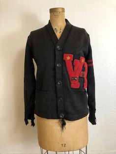 "Vintage 1950's letterman cardigan sweater. Nicely worn and faded. Buttons down the front. Two hip pockets. Double red stripe on one sleeve. \"VH\" red patch. Both sleeves are pretty holey and need repair. There are a few holes on the front, underarm, and back. There is also some unraveling on the front underneath the bottom button. This sweater has a lot of character and is being sold as is. . M E A S U R E M E N T S. measured laying flat, please multiply by two Shoulder to shoulder: 17 inches Black Retro Cotton Cardigan, Vintage Sweater With Pockets For Fall, Vintage Fall Sweater With Pockets, Retro Cotton Cardigan For College, Retro Cotton Cardigan, Vintage College Sweater For Fall, Vintage College Sweater For Winter, Vintage Sweater For College In Fall, Vintage Sweater For College In Winter