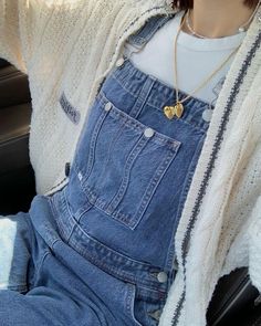 a woman wearing overalls and a sweater is sitting in the back seat of a car