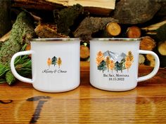 two white mugs sitting on top of a wooden table next to some wood logs