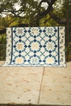 a blue and white quilt sitting on top of a wooden table next to a tree