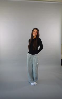 a woman standing in front of a gray background with her hands on her hips and smiling at the camera