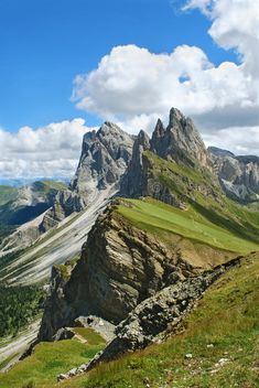 the mountains are covered in green grass and rocks, with some clouds above them on a sunny day