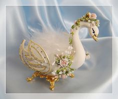 a white swan figurine with flowers on it's head and feathers around its neck