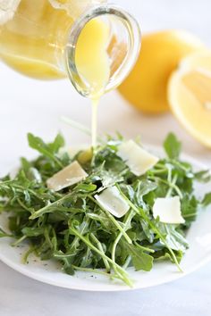 someone is pouring dressing into a salad on a plate with lemons and parmesan cheese