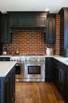 a kitchen with black cabinets and white counter tops, an oven and stove top in front of a brick wall