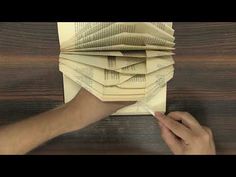 a person holding a pen over a stack of books on top of a wooden table