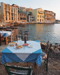 an outdoor table with food on it next to the water in front of some buildings