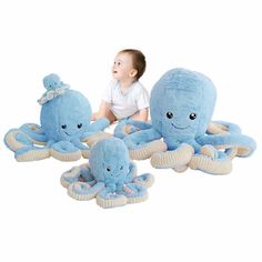 a baby sitting on the ground next to three stuffed octopus toys, one blue and one white