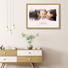 a couple kissing in front of a white wall with a wooden dresser and potted plant