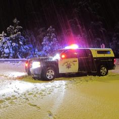 two police trucks parked in the snow at night time with lights on and trees behind them