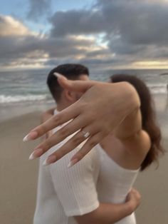 a man and woman standing on top of a beach next to the ocean with their hands in the air