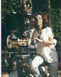 a woman sitting in front of a camera on top of a wooden table next to other people