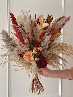 a person holding a bouquet with dried flowers and feathers in front of a white door