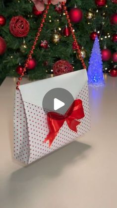 an origami bag with a red bow hanging from it's side on a table in front of a christmas tree