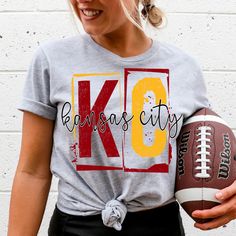 a woman holding a football and wearing a kansas city t - shirt with the word kc on it