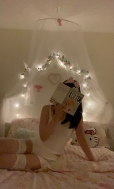 a woman laying in bed reading a book with fairy lights on the headboard behind her