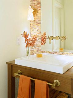 a bathroom sink with two orange towels hanging from it's hooks and a mirror in the background