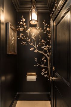 a bathroom with black walls and white flowers on the wall next to the toilet paper dispenser