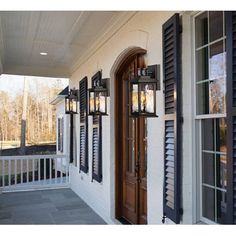 the front porch is decorated with black shutters and two lanterns on each side of the door