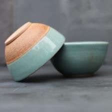 two green bowls with wooden lids sit side by side on a gray surface, next to each other